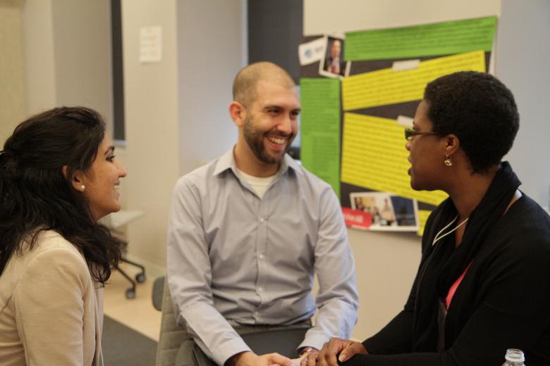 في هذه الصورة ثلاثة معلمين يرتدون ملابس عمل غير رسمية ويجلسون في الداخل على شكل مثلث، ويواجه كل منهم الآخر، والمعلمة التي ترتدي نظارات على أقصى اليمين هي من تتحدث، بينما يبتسم ويضحك المعلمان الآخران، وتوجد لوحة معلقة في الخلفية تحتوي على مجموعة من الصور والنصوص.