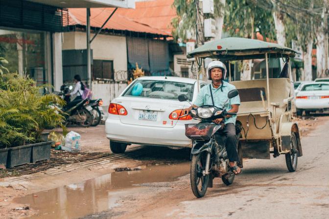 Man Riding Motorcycle Near White Car, Krong Siem Reap, Siem Reap Province, Cambodia