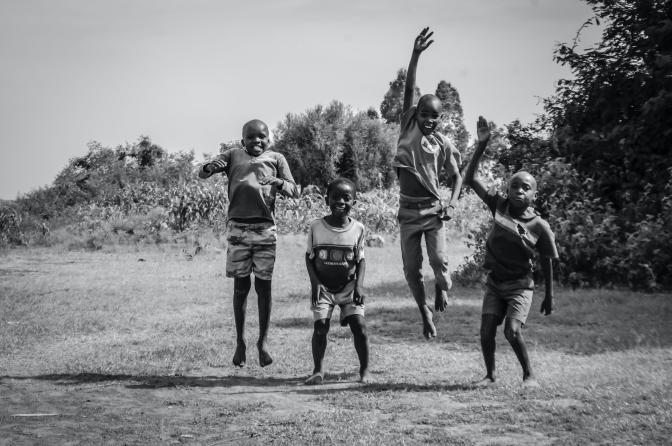 Grayscale Photo of Children Jumping on the Grass Field