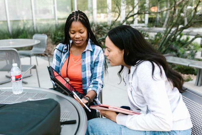 Two young women looking at an iPad together sitting outside