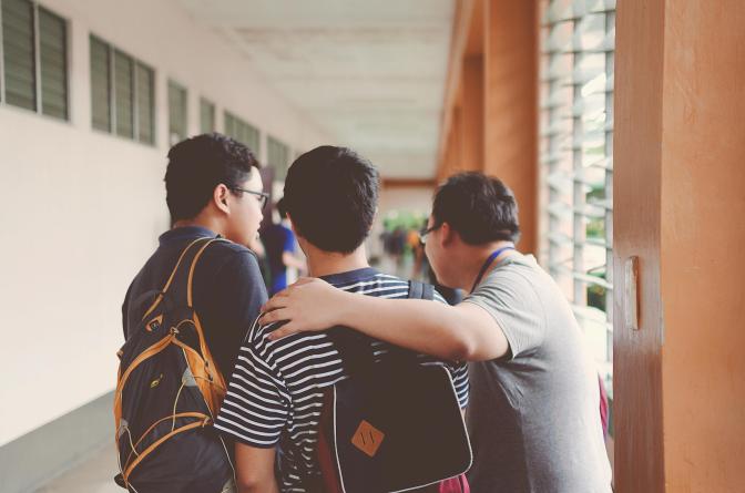 Three male students standing in the hallway with one resting his arm over another