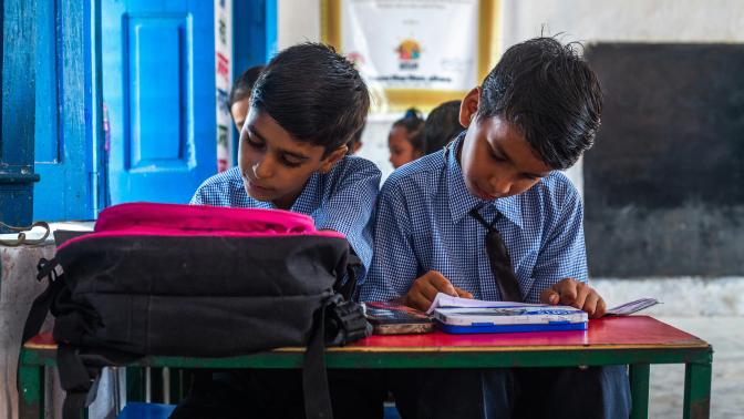 two boys sitting at a table in a classroom