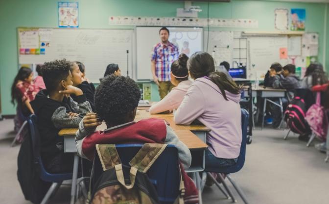 teacher in front of a classroom with students listening