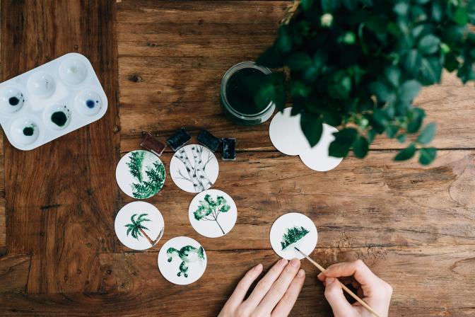 hands painting trees on small circular cardboards