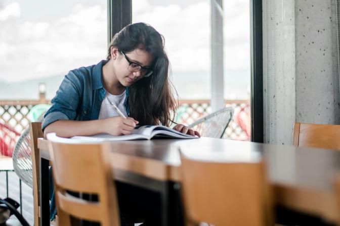 student wearing glasses writing in a notebook