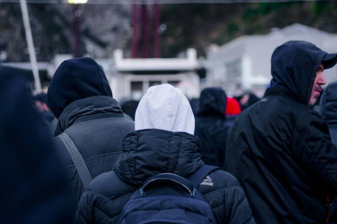 Backs of refugees in winter coats wearing backpacks