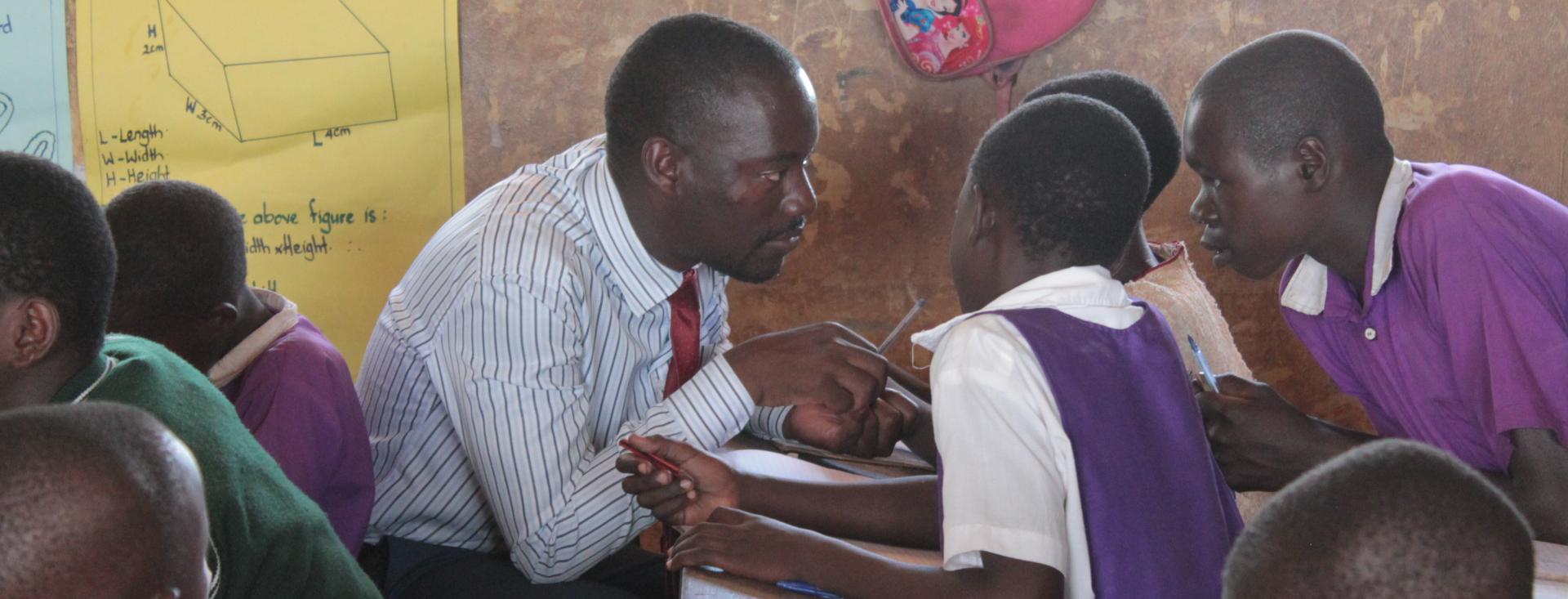 Teach For Uganda teacher sitting and guiding his students