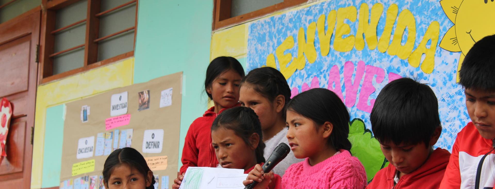 في الصورة مجموعة من الأطفال الذين يقدّمون مشروعهم حول كيفية مكافحة فقر الدم في مجتمعهم، ويوجد طفلة في وسط المجموعة تتحدث في ميكروفون تمسكه بيدها، وطفلة على يسارها ترفع رسومات ليراها الجمهور، وتنظر الطفلة المجاور لها إلى المتحدثة، وتظهر في الخلفية لوحات عرض ملوّنة.