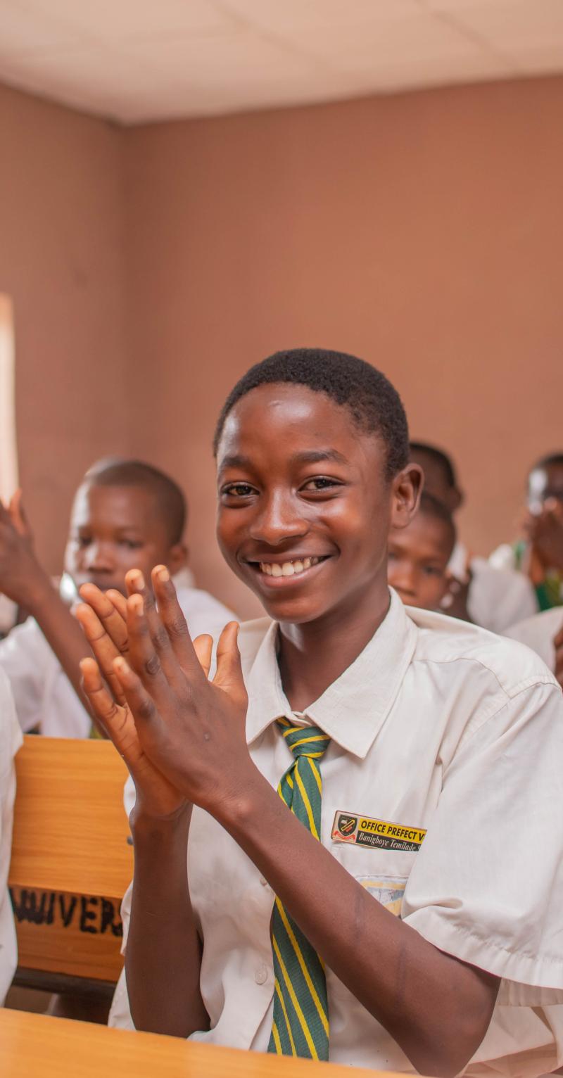 Des élèves portant l'uniforme de leur école sont assis sur des bancs en classe et applaudissent.