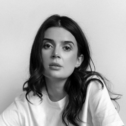 Black and white portrait shot of Larisa Hovannisian, a woman with long, dark hair who is looking at the photographer with a neutral expression.